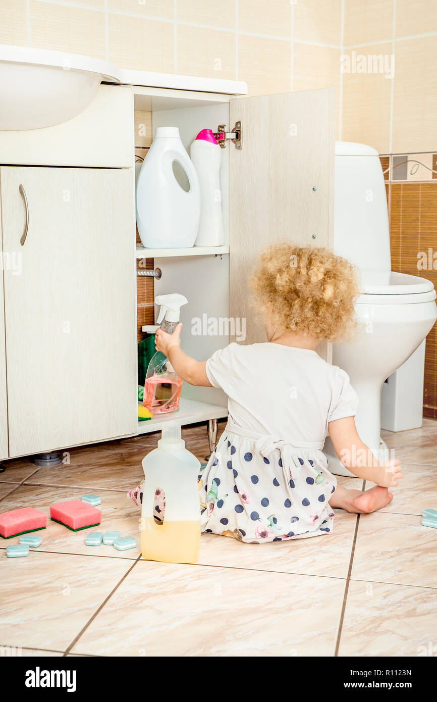 Unattended girl child play quietly at bathroom with dangerous household chemicals. Safety hazard at home concept. Keep away from children`s reach. Stock Photo